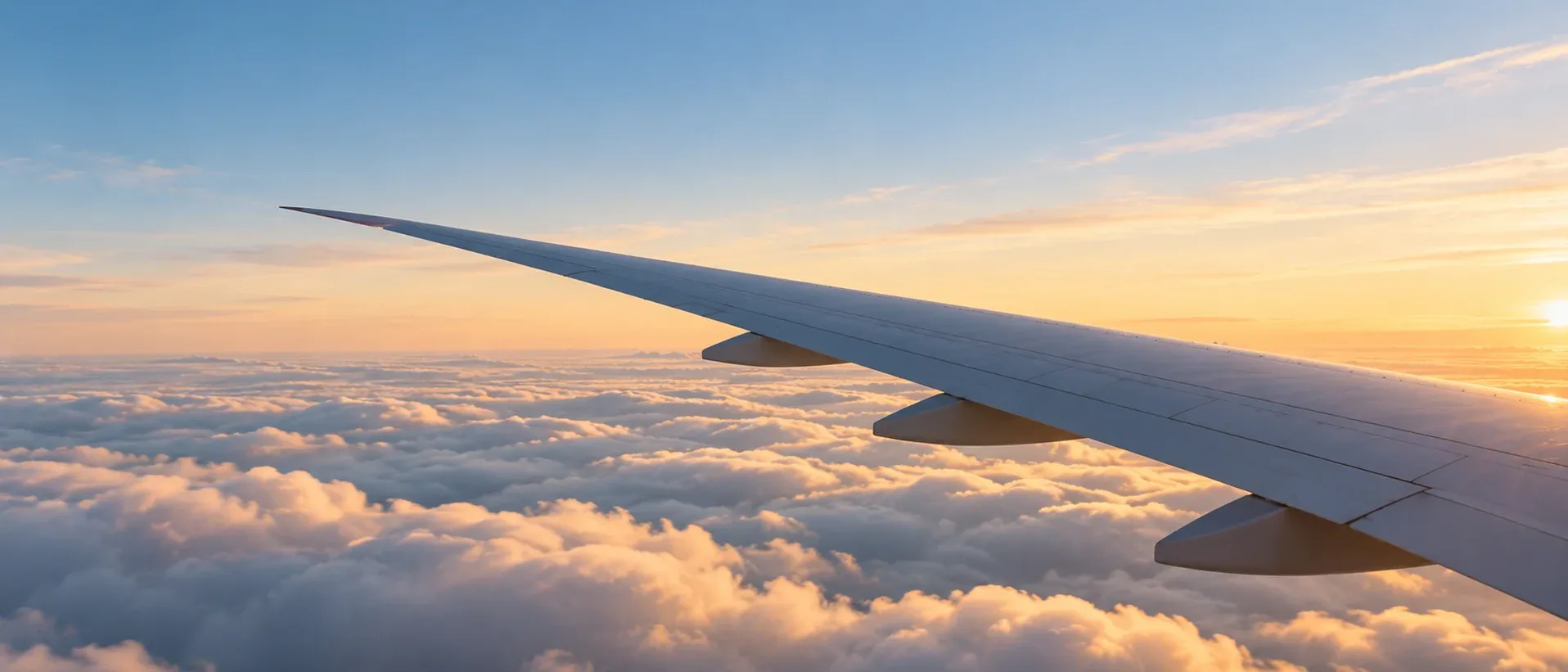 Aircraft wing above an unbroken layer of cloud in daylight, seen from a cabin window